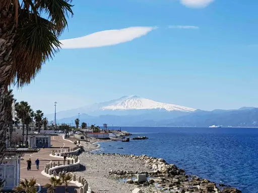 Lungomare di Reggio Calabria con vista sull'Etna innevato. Perfetto per scoprire cosa visitare a Reggio Calabria, tra palme e mare blu.
