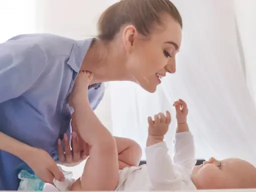 Uśmiechnięta mama zmienia pieluchę dziecku, zapewniając mu komfortowe szerokie pieluchowanie bioderek.