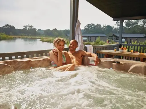 A happy couple enjoys a hot tub with a view of a serene gay lake.