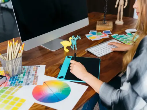 Kreatywna przestrzeń: graficzka przy biurku z tabletem graficznym, próbkami kolorów i komputerem. Idealne miejsce do tworzenia sitodruk grafika.