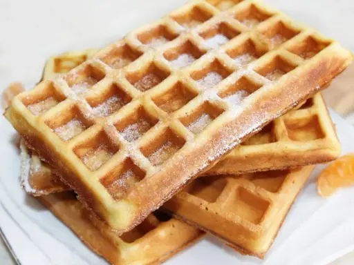 Stos świeżo upieczonych gofrów, posypanych cukrem pudrem. Idealne ciasto na gofry, które zachwyci każdego.