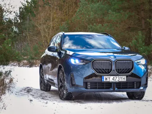 Niebieskie, nowe BMW X3 na ośnieżonej drodze w lesie. Zimowe opony gotowe na wyzwania.