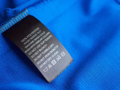 Tvättlapp på blått tyg visar 100% polyester. Skillnaden mellan polyamid vs polyester är viktig för skötselråden.