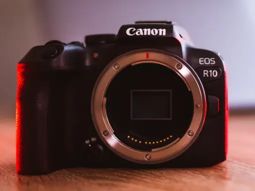 Canon EOS R10 w teście. Ciemna obudowa aparatu z czerwonym podświetleniem, widoczny bagnet obiektywu.