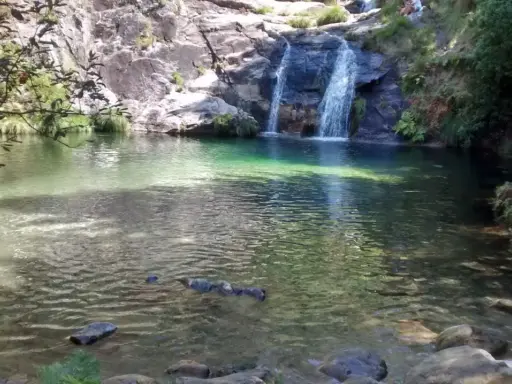 Un hombre disfruta de las pozas de Mougas, con cascadas cayendo sobre rocas y vegetación exuberante.