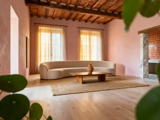 Salon aux murs roses, canapé courbe, table basse en bois et tapis en jute. Une ambiance douce et harmonieuse pour une maison feng shui.