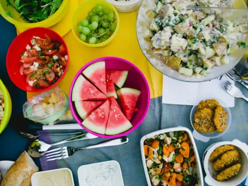 Bunte Schüssel mit Wassermelone, Kartoffelsalat, Trauben und Tomatensalat – leckere Picknick-Snacks für einen sonnigen Tag.