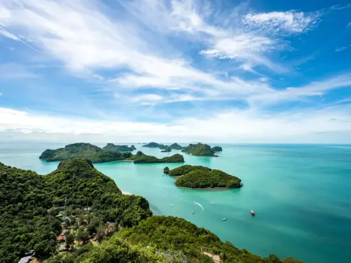 Grüne Inseln ragen aus türkisfarbenem Wasser im Nationalpark Thailand. Kleine Boote gleiten über die ruhige See unter einem blauen Himmel mit weißen Wolken.
