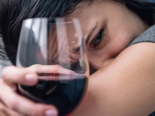 Smutna twarz kobiety z kieliszkiem wina. Czy to jeden z 6 objawów uzależnienia od alkoholu?
