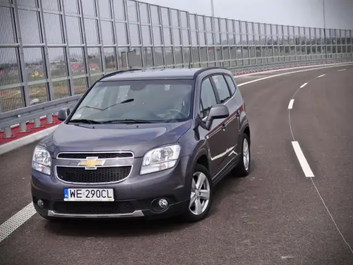 Szary Chevrolet Orlando 1.8 benzyna na pustej drodze, za barierami dźwiękochłonnymi.