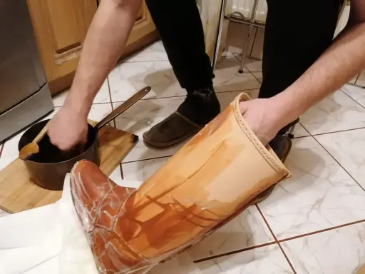 Domowy sposób na impregnację butów: ręka zanurza drewnianą łyżkę w garnuszku z preparatem, by nałożyć go na skórzany but.