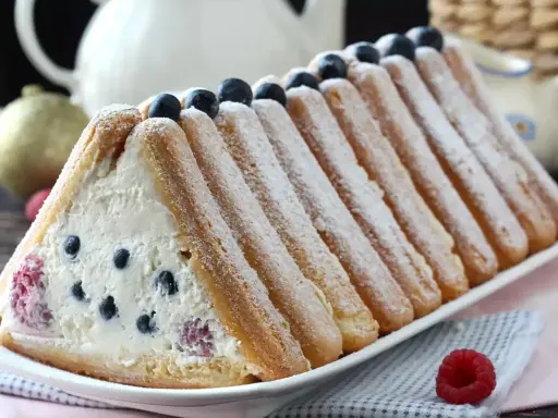Délicieuse recette buche fruits rouges : un gâteau léger garni de crème et de baies, entouré de biscuits à la cuillère saupoudrés de sucre glace.