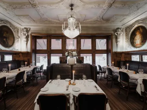 Elegant dukade bord med levande ljus i en av Stockholms gamla restauranger. Kristallkrona och konst pryder taket.