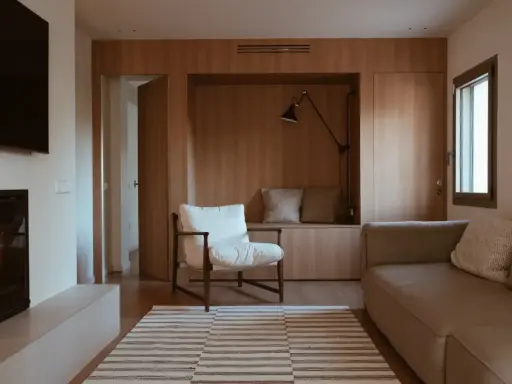 Salones pequeños con mueble de madera integrado, sofá, sillón blanco y alfombra a rayas.