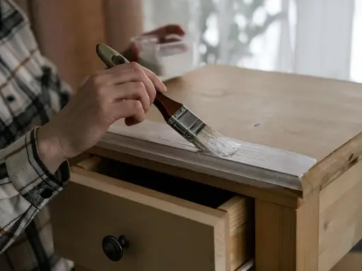 Mano con pincel aplicando pintura blanca para pintar madera de un mueble.