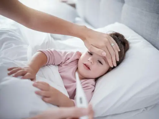 Mama sprawdza temperaturę chorego dziecka, martwiąc się przegrzaniem.