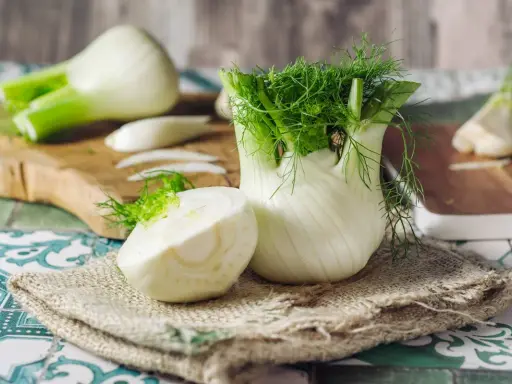 Fenouil frais, prêt à révéler ses bienfaits. Une moitié coupée montre sa texture croquante, tandis que le bulbe entier déploie ses feuilles aériennes.