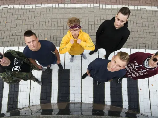 Grupa młodych ludzi, jakby szukających weny raperów, stoi na pasach.