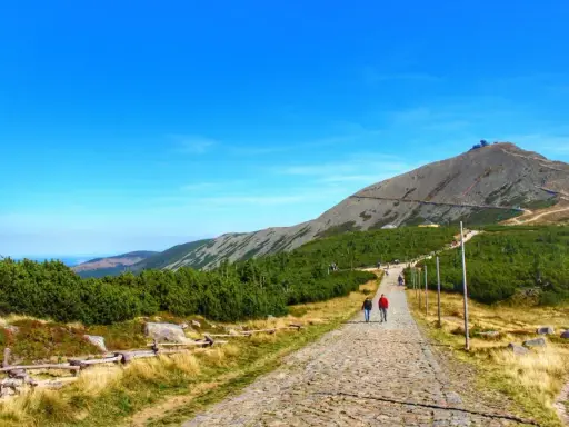 Kamienista ścieżka prowadzi na szczyt Śnieżki. Turyści idą w kierunku górskiej panoramy.