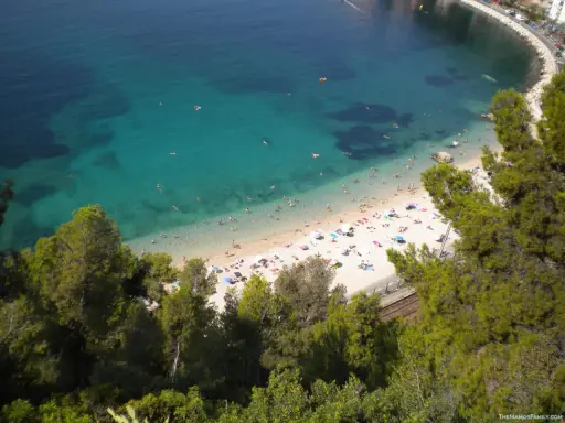 Spiaggia affollata sulla costa azzurra con bambini che giocano in acqua e prendono il sole.