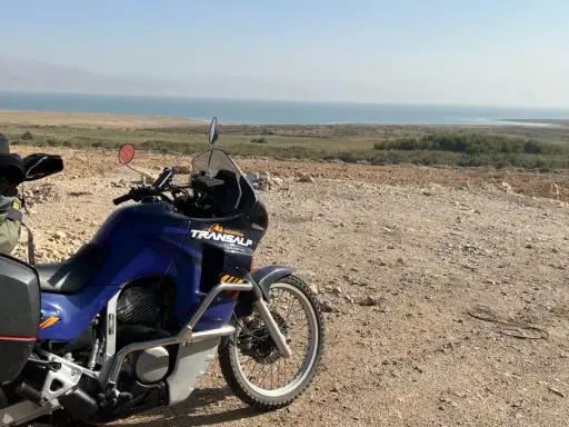 Motocykl Honda Transalp z bagażami gotowy do podróży, z widokiem na Morze Martwe. Dokumenty, jak **carnet de passage**, czekają na przygodę.