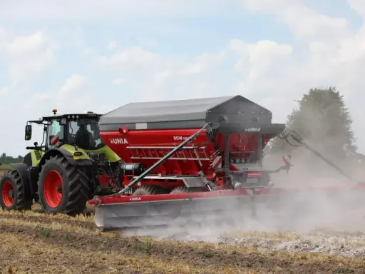 Traktor z rozsiewaczem wapna RCW 1300 marki UNIA na polu. To idealne rozwiązanie, jakie wapno pod warzywa, by zapewnić im najlepsze warunki do wzrostu.