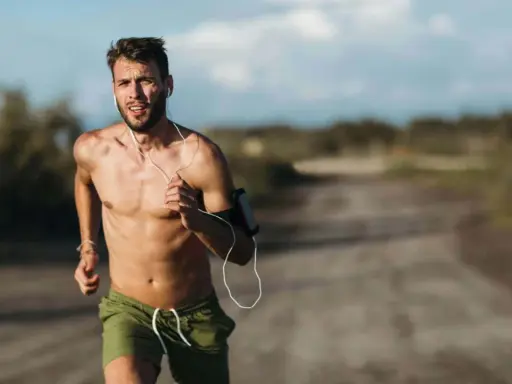 Ein Mann läuft bei Hitze, sein Puls rast. Er trägt Kopfhörer und eine Armbinde für sein Handy.