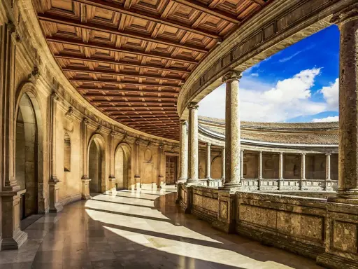 Ein sonnenbeschienener Arkadengang mit kunstvoller Holzdecke und Säulen, der zum Innenhof der Alhambra Moschee führt.
