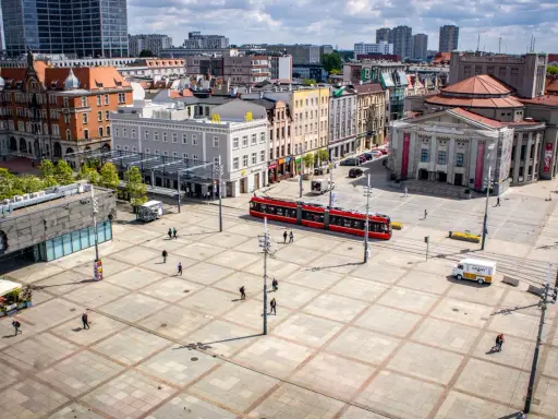 Rynek w Katowicach z czerwonym tramwajem i ludźmi spacerującymi po placu. Idealne miejsce na odkrywanie katowickich atrakcji dla młodzieży.
