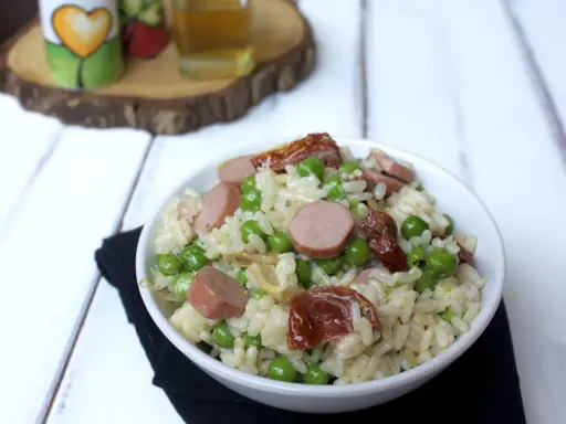Una ciotola di insalata di riso con piselli, salsiccia e pomodori secchi, pronta per essere gustata.
