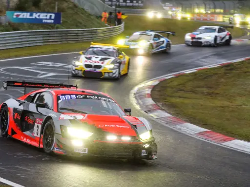 Un Audi R8 rojo y negro compite en las 24 Horas Nürburgring, con otros coches de carreras en la pista mojada.