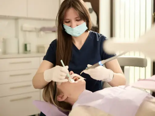Dentystka w masce i rękawiczkach wykonuje zabieg stomatologiczny u pacjentki.
