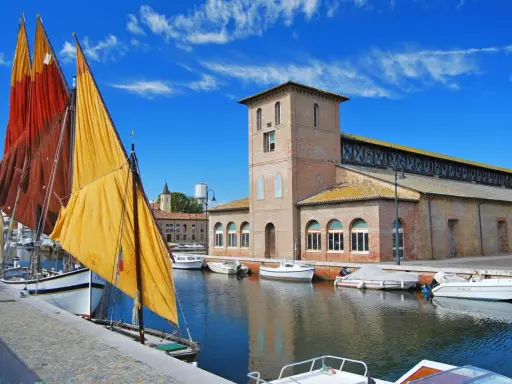 Vele colorate di barche tradizionali ormeggiate nel porto canale di Cervia mare, con l'antico edificio delle saline sullo sfondo.