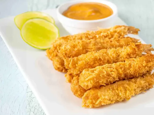 Crujientes gambas a la gabardina doradas, servidas con rodajas de lima y una salsa cremosa.