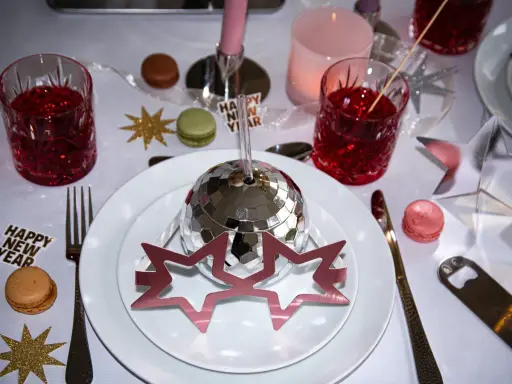 Enkel nyårsdukning med disco-boll, stjärnor, macarons och röda drinkar. En festlig och glittrig bordsdekoration för att fira in det nya året.