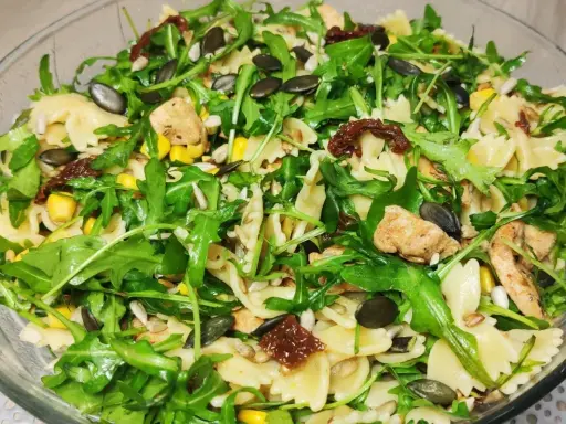 Kolorowa sałatka z makaronem farfalle, rukolą, kurczakiem, kukurydzą i słonecznikiem, wzbogacona o intensywny smak suszonych pomidorów.