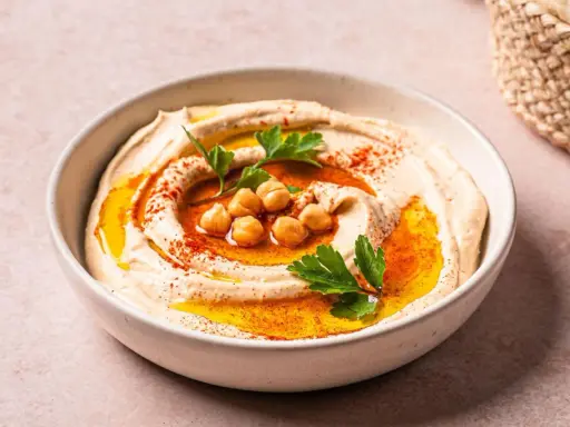 Cremiger Hummus in einer Schüssel, garniert mit Kichererbsen, Petersilie und Paprikapulver. Ein köstliches Gericht mit Hummus, bereit zum Genießen.