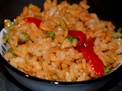 Un bol de riz coloré avec des petits pois et des poivrons rouges, parfait pour une recette salade riz facile et rapide.