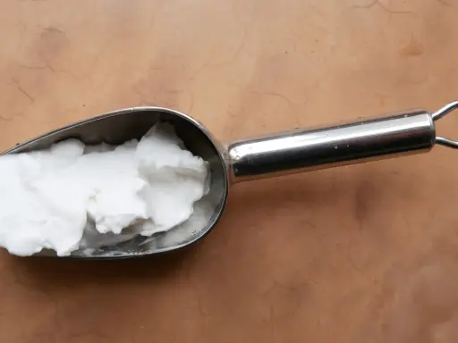Une cuillère métallique contient une pâte blanche, peut-être de la cire saponifiée sur enduit chaux, prête à être appliquée.