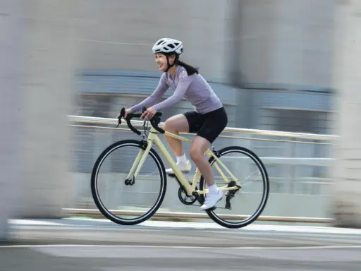 Uśmiechnięta kobieta w kasku pędzi na rowerze, ciesząc się sportami rowerowymi.