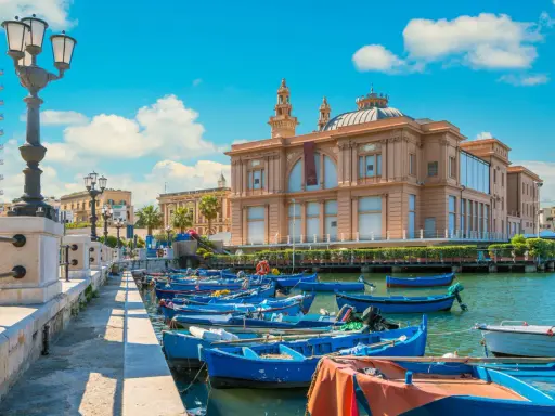 Barche blu ormeggiate nel porto di Bari, con il Teatro Margherita sullo sfondo. Un'immagine che cattura l'essenza di cosa vedere a Bari.