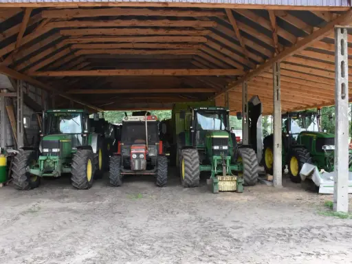 Kilka zielonych i jeden czerwony traktor stoją pod drewnianą wiatą. To pewnie ich tymczasowe schronienie, bo taka wiata bez pozwolenia to nie najlepszy pomysł.