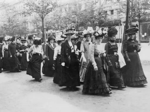 Frauen in langen Kleidern und Hüten marschieren entschlossen. Ein historisches Bild der feministischen Bewegung.