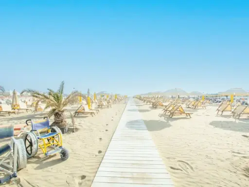 Una passerella bianca conduce alle spiagge di Riccione, con sdraio e ombrelloni pronti per accogliere tutti, compresa una sedia a rotelle speciale per la sabbia.