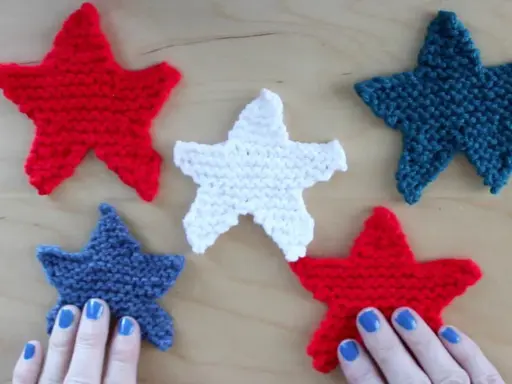 Cinco estrellas tejidas de punto estrella, rojas, blancas y azules, dispuestas sobre una superficie de madera.