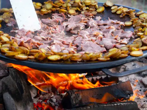 En stor stekpanna över öppen eld där kött och potatis tillagas. En perfekt dag att laga mat ute!