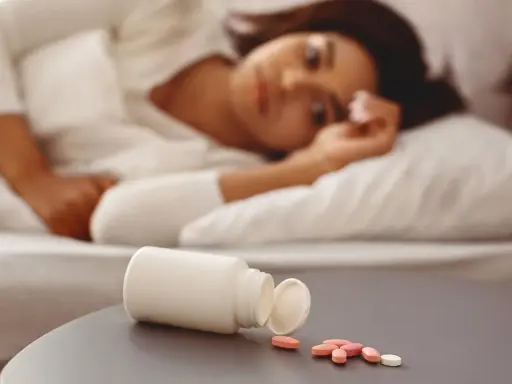 Frau liegt im Bett, daneben eine offene Pillendose mit Tabletten. Vielleicht die Suche nach Schlaf mit Melatonin maximaldosis.