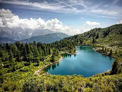 Laghi di San Giuliano: un'oasi alpina con acque turchesi, circondata da fitti boschi di conifere e montagne maestose sotto un cielo azzurro con nuvole bianche.