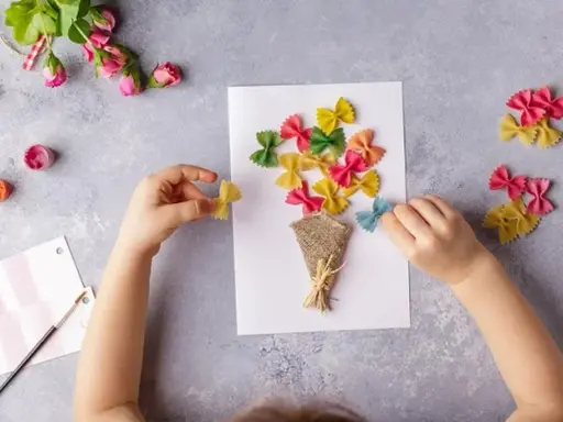 Dziecko tworzy bukiet z kolorowego makaronu farfalle na laurce. Świetne pomysły na laurki!