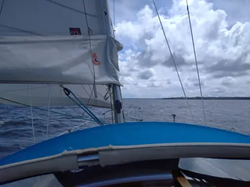 Vue depuis un voilier, le **lofer voile** blanc gonflé par le vent, sur une mer agitée sous un ciel nuageux.
